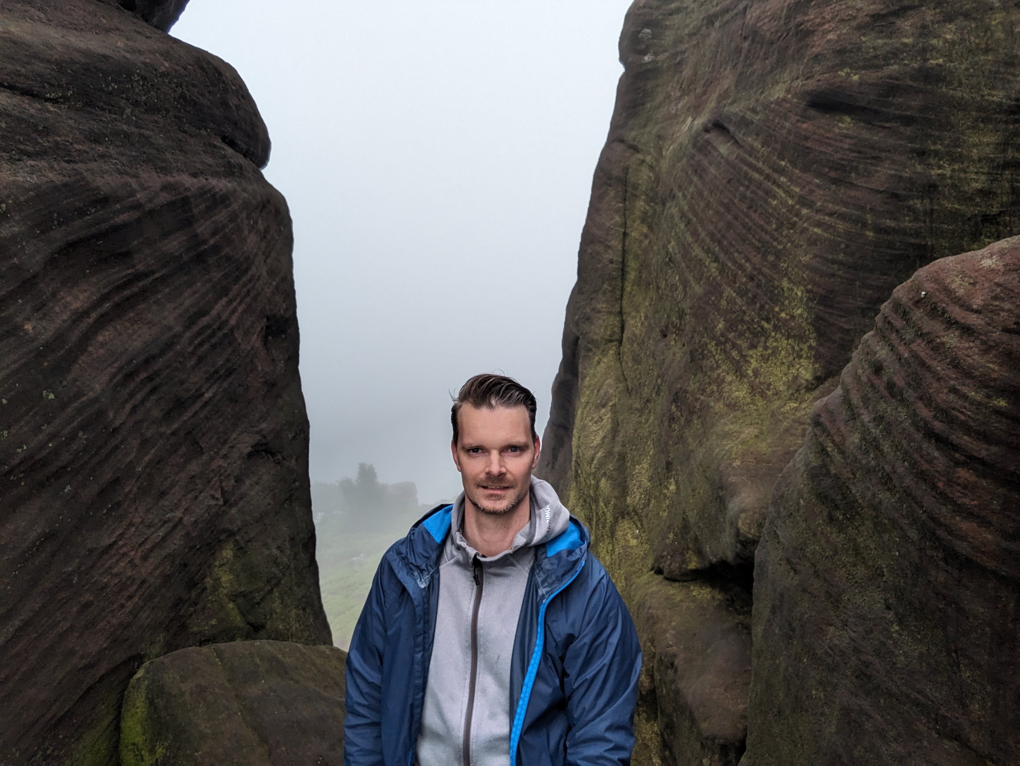 darren standing at the top of hen cloud between two stones with fog all around